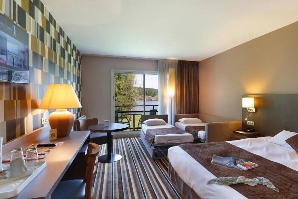 Een hotelkamer met een bed, twee nachtkastjes, een bureau met stoel, een kleine tafel met stoel, een lamp en uitzicht op de omgeving.