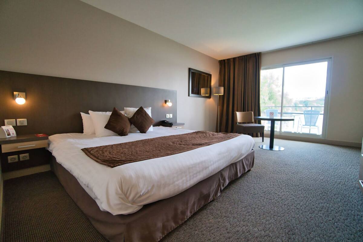 Een hotelkamer met een groot bed, een bureau met een lamp, een stoel en uitzicht op de omgeving.