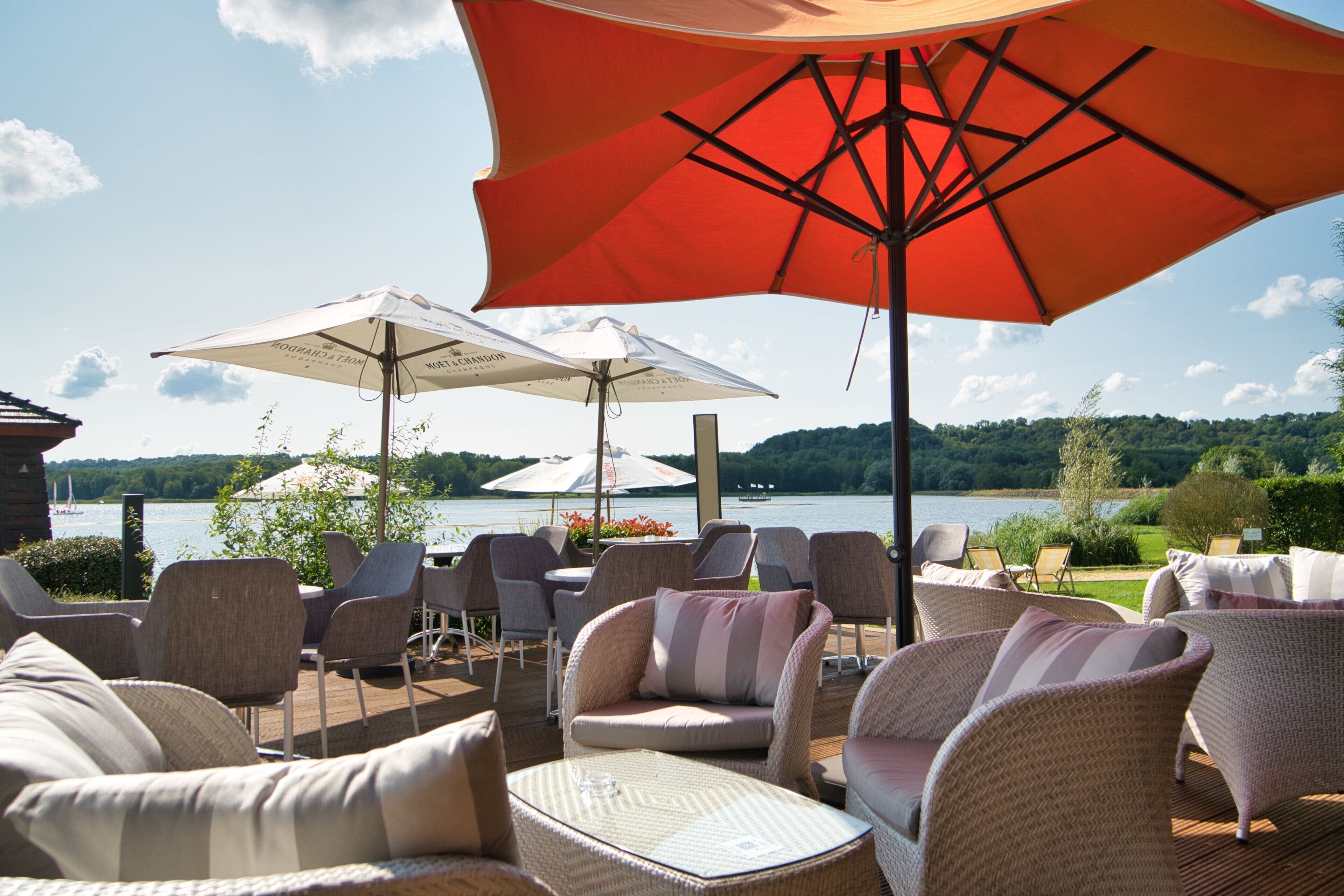 An outdoor seating area with wicker furniture and umbrellas, overlooking a lake.