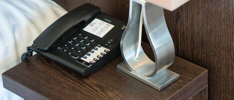 A bedside table with a lamp, a telephone, and a small drawer.
