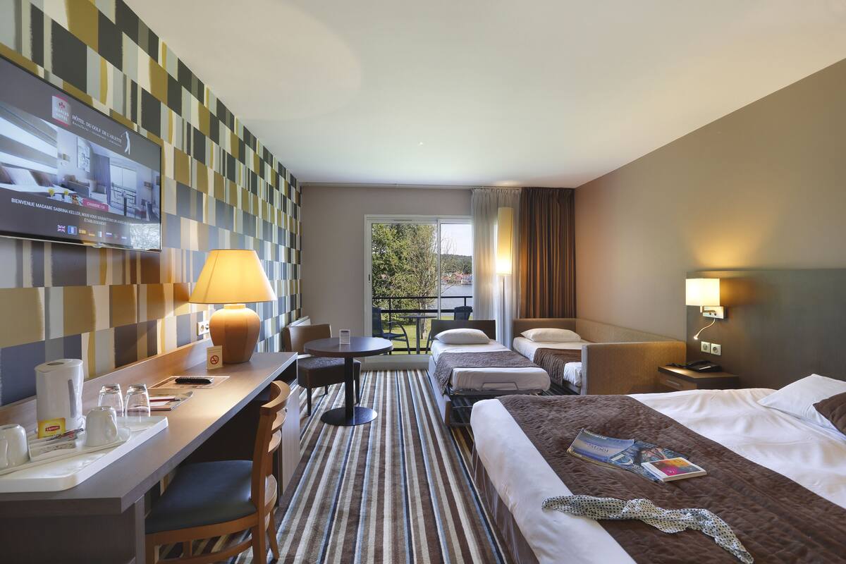 Een hotelkamer met een televisie, bureau, stoelen, een bed, nachtkastjes en uitzicht op de omgeving.