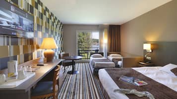 A hotel room with a TV, desk, chairs, a bed, bedside tables, and a view of the outdoors.