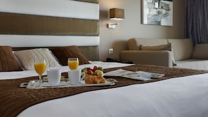 Une chambre d’hôtel avec un lit soigneusement fait, un plateau de petit-déjeuner avec des croissants et des fruits, et une lampe fixée au mur.