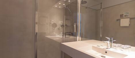 Un baño moderno con ducha de vidrio, un espejo grande y un lavabo blanco.