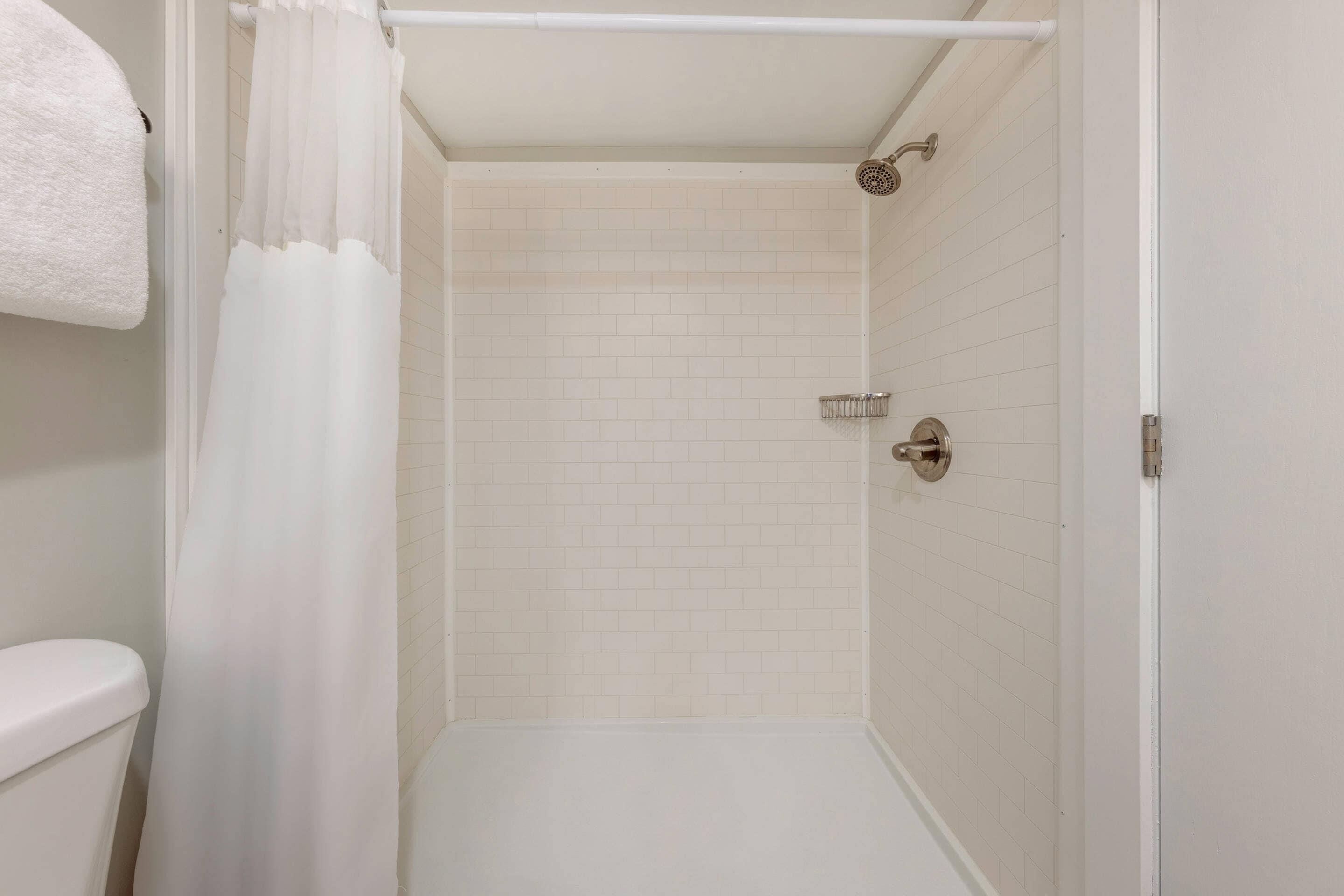 A small, white-tiled shower room with a showerhead, a towel rack, and a toilet.