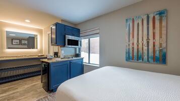 A modern hotel room with a large bed, a kitchenette, a microwave, and a painting of skis on the wall.