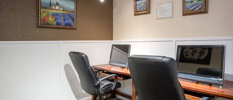 A conference room with a wooden table, two black office chairs, and three framed paintings on the wall.