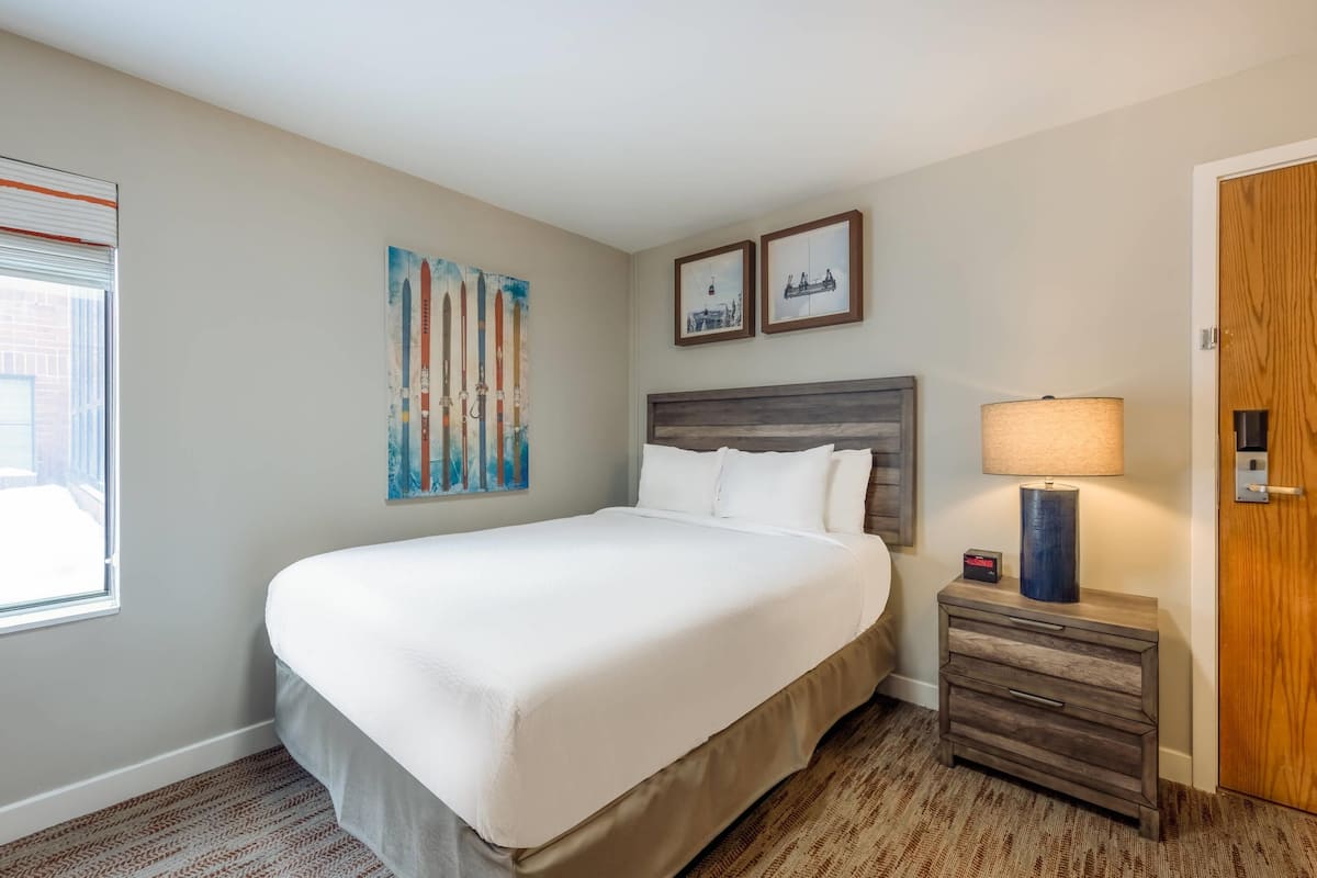 Een hotelkamer met een groot bed, een nachtkastje met een lamp en twee ingelijste foto's aan de muur.