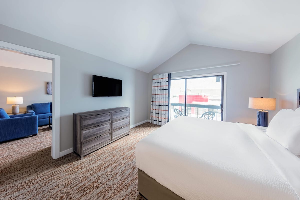 Een hotelkamer met een groot bed, een televisie, een dressoir, een blauwe bank en een balkon met uitzicht.