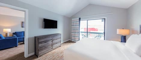 Habitación de hotel con una cama grande, un televisor, un aparador, un sofá azul y un balcón con vistas.