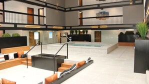 Een ruime lobby met een zwembad, meerdere zithoeken en een trap naar de verdiepingen erboven.