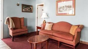 A living room with a red sofa, a matching armchair, and a small wooden coffee table. There is a framed picture on the wall and a lamp on a side table. - Villa Inn (Lawrenceburg)
