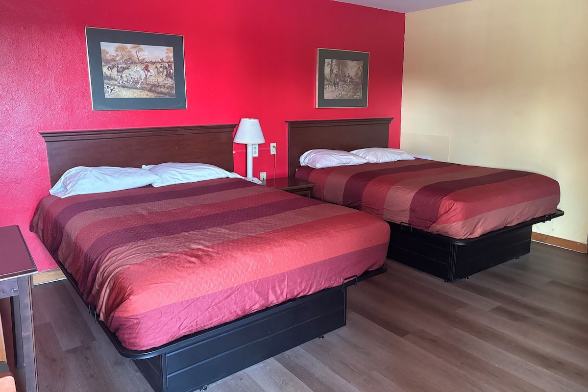 A hotel room with two beds, each with a red-striped bedspread, wooden headboards, and two framed pictures on the walls.