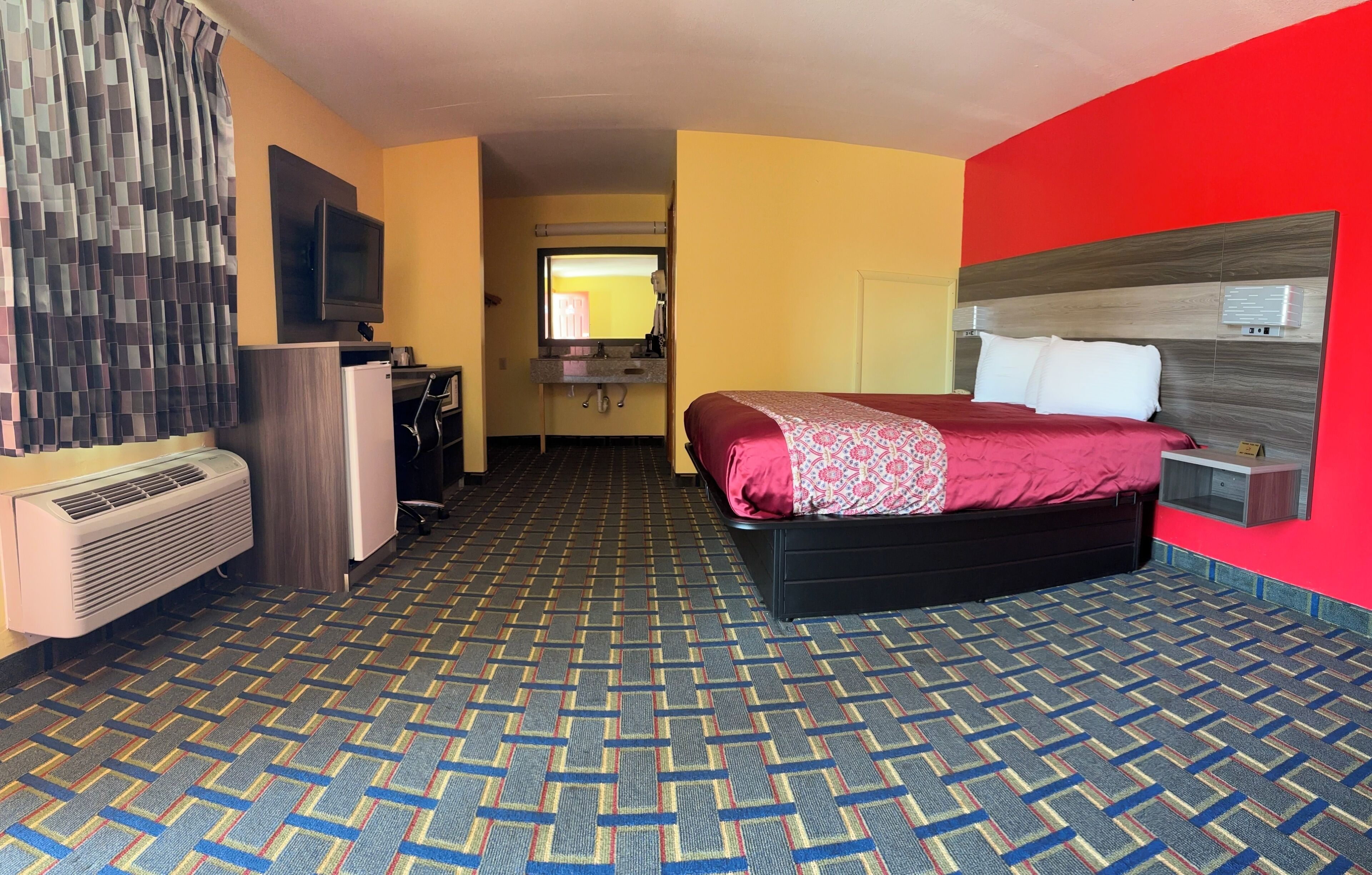 A hotel room with a bed, a TV, a desk, and a mirror.