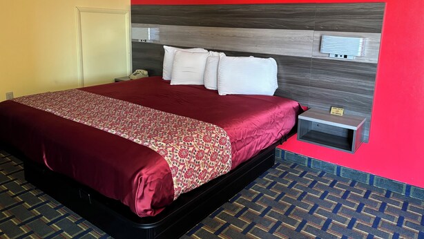 A hotel room with a bed, a nightstand, a telephone, and a wall-mounted control panel. - Villa Inn (Lawrenceburg)