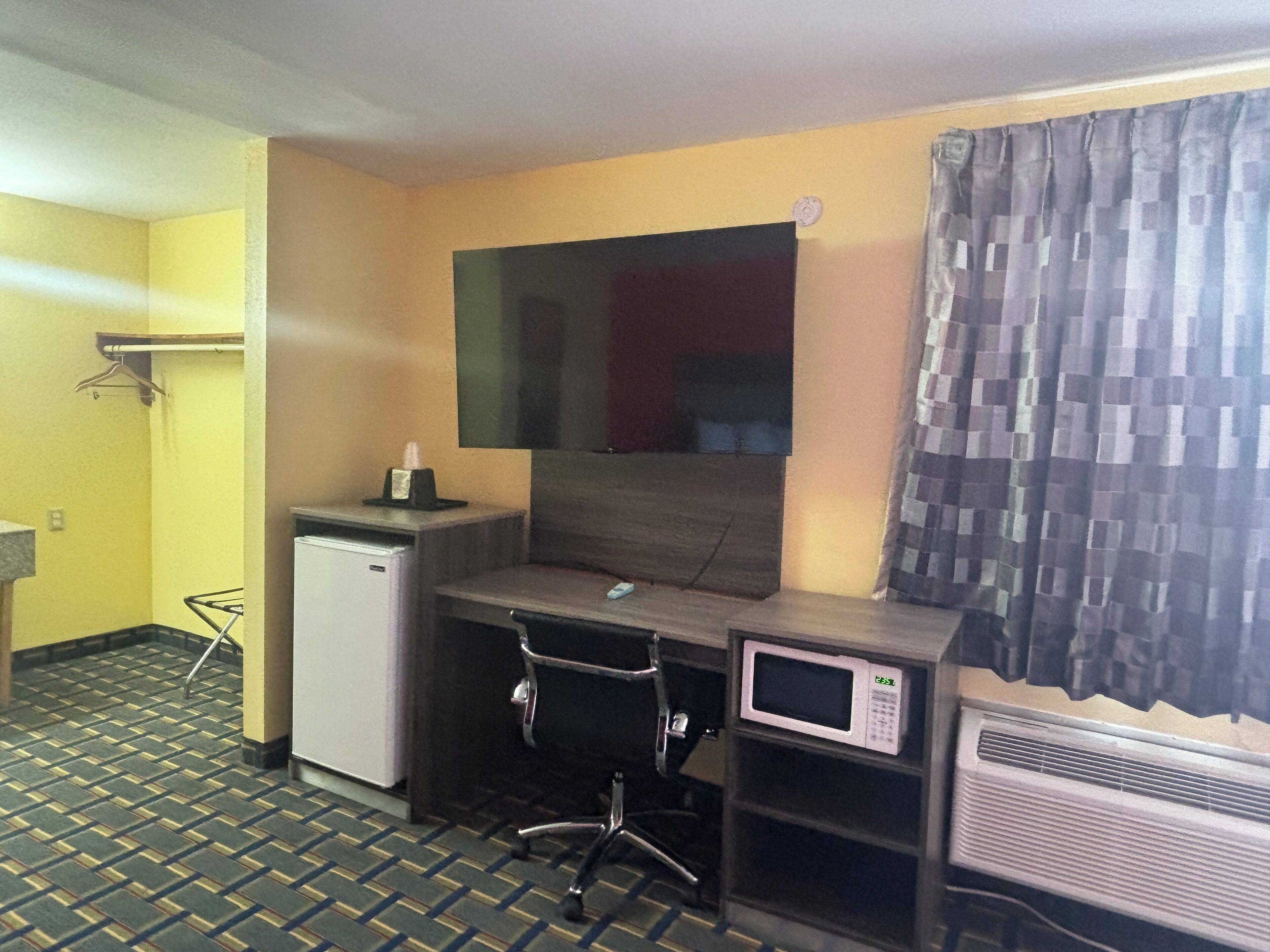 A compact hotel room with a small desk, a microwave, and an air conditioner.