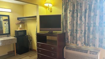 A hotel room with a wooden dresser, a flat-screen TV, a microwave, a heater, and a mirror.