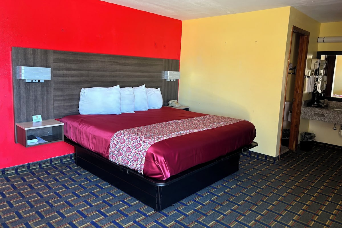 A hotel room with a large bed, a headboard with a built-in phone, a bedside table, and a bathroom visible through an open door.