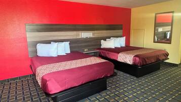 A hotel room with two beds, each with a red bedspread and white pillows. The room has a red wall and a patterned carpet.