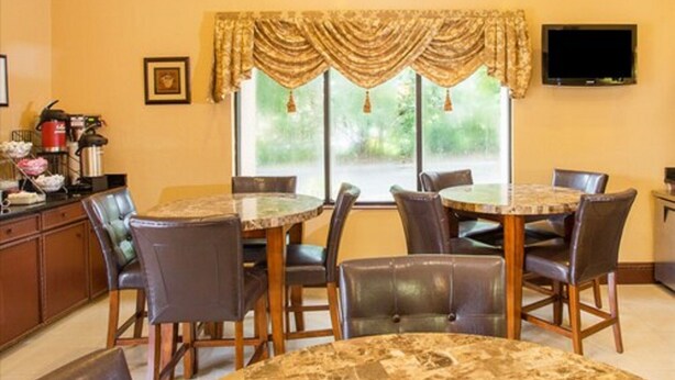 Un comedor con una mesa redonda y sillas, una ventana con cortinas, un televisor en la pared y una cafetera en la encimera.