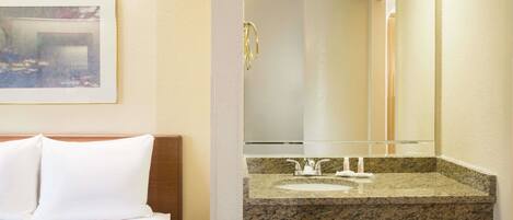 A hotel room with a bed, a bathroom with a granite countertop sink, and a framed picture on the wall.