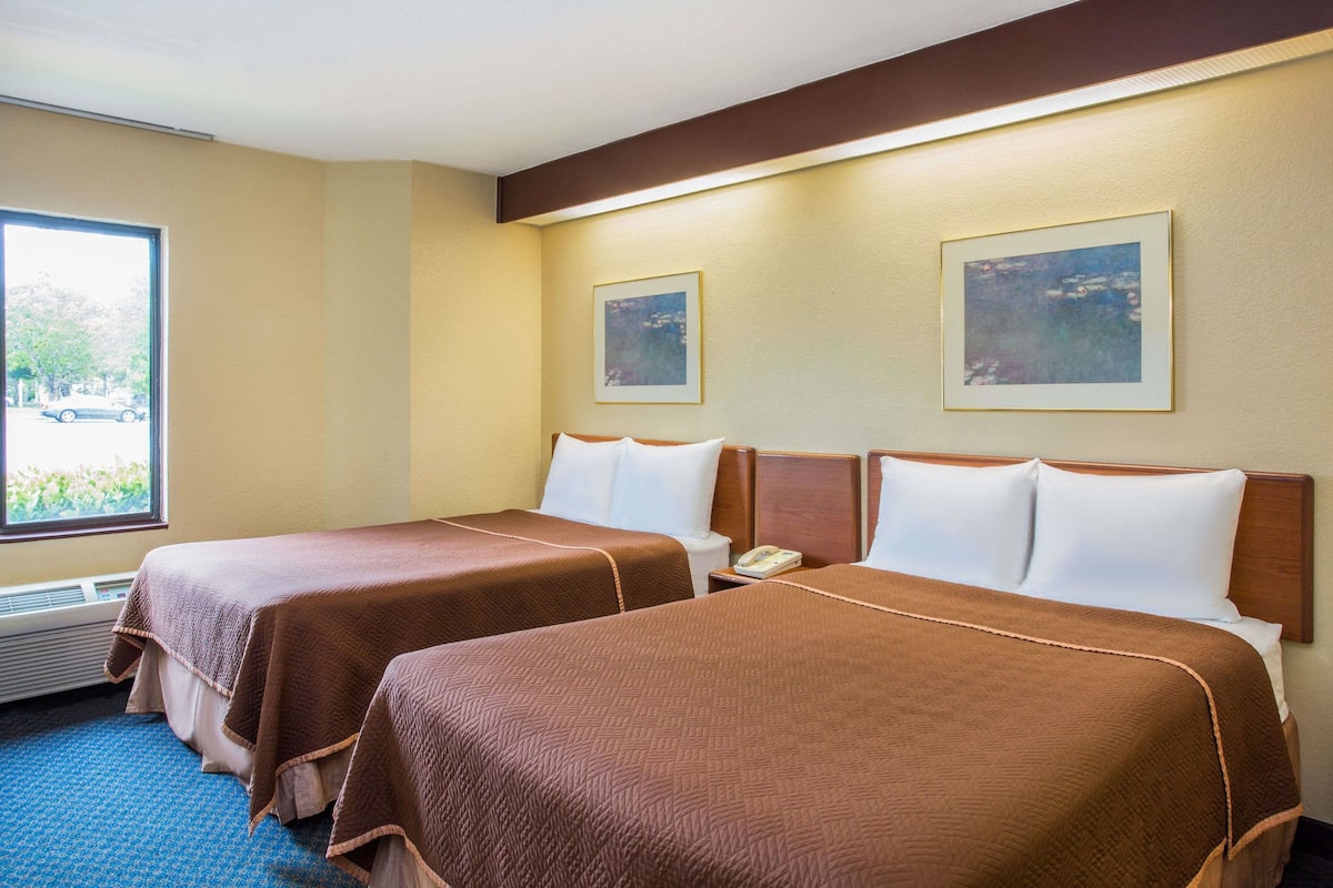 Une chambre d’hôtel avec deux lits, une fenêtre donnant sur l’extérieur et deux tableaux encadrés accrochés au mur.