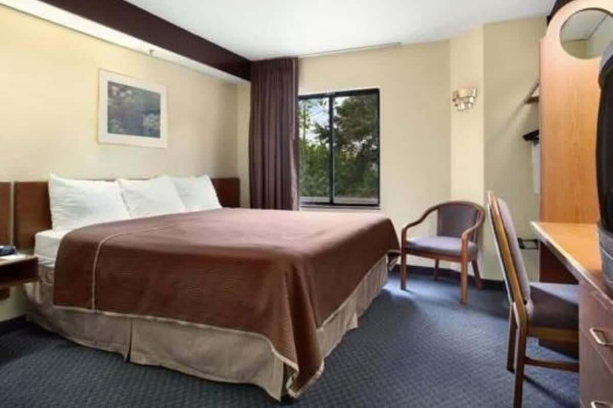 Une chambre d’hôtel avec un lit, un bureau, une chaise, une fenêtre et un tableau au mur.