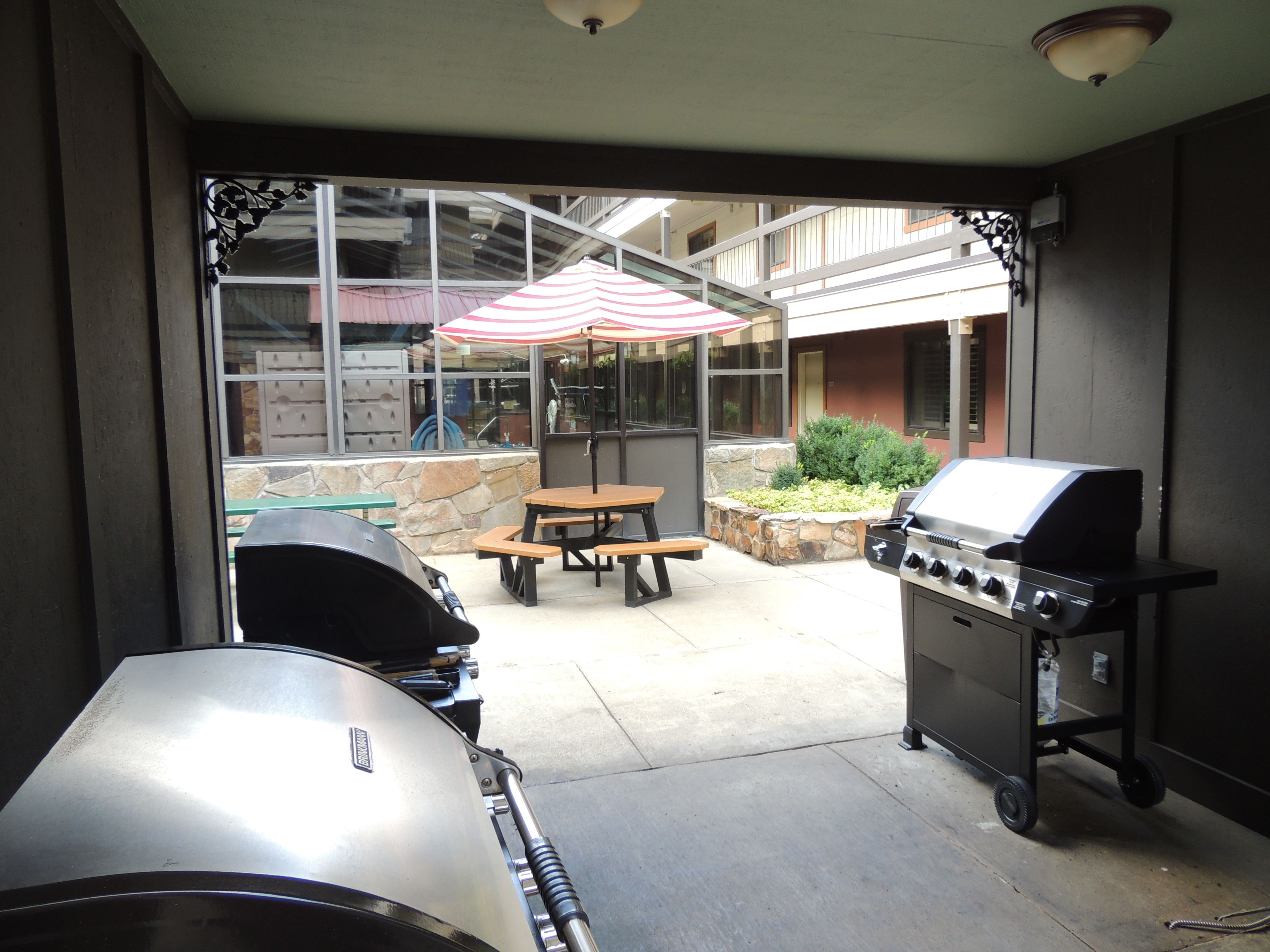 Un área de patio al aire libre con una parrilla, una mesa de picnic y una sombrilla.