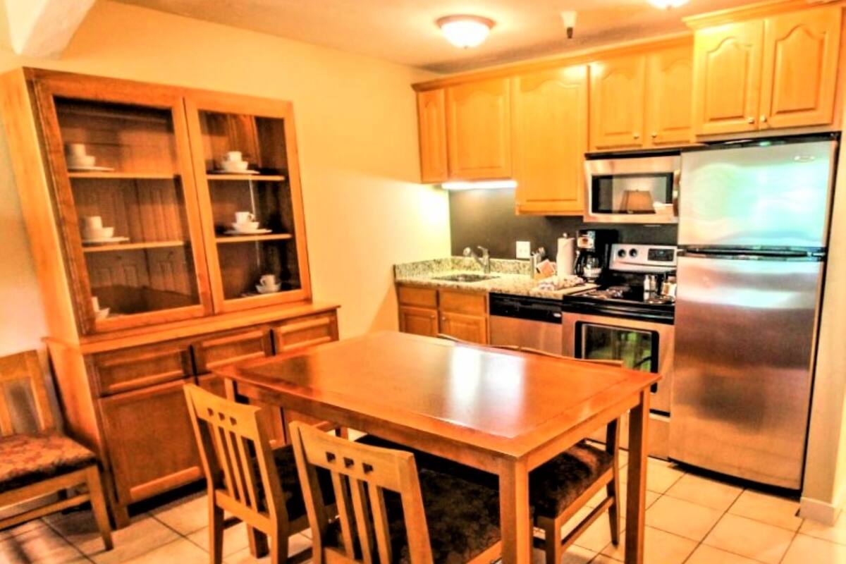Una cocina compacta con armarios de madera, un refrigerador de acero inoxidable, un microondas y una estufa.