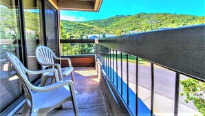 A balcony with two white plastic chairs, a glass door, and a view of a road and green hills. - Park Regency Resort (Park City)