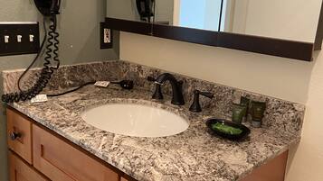 Un bagno con lavabo in granito, uno specchio, un asciugacapelli e un portasciotto.
