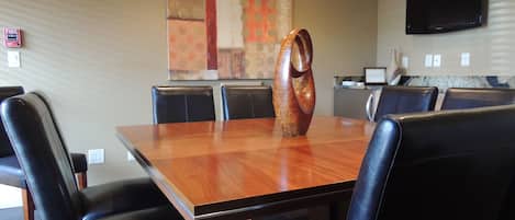 Un salón de conferencias con una mesa de madera, sillas de cuero negro, un jarrón decorativo, un cuadro en la pared y un televisor de pantalla plana sobre la mesa.