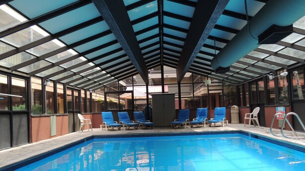 An indoor swimming pool with clear blue water, surrounded by lounge chairs and a glass ceiling structure. - Park Regency Resort (Park City)