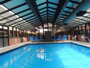 An indoor swimming pool with clear blue water, surrounded by lounge chairs and a glass ceiling structure. - Park Regency Resort (Park City)