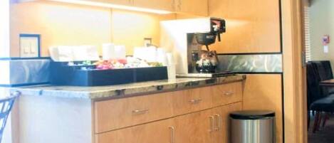 A compact kitchen with wooden cabinets, a stainless steel trash bin, and a countertop with a coffee maker.