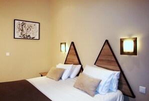 Habitación de hotel con una cama grande, dos mesitas de noche y una lámpara fijada a la pared.