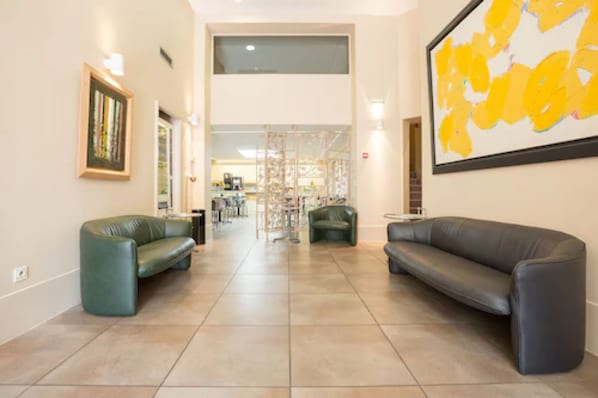 A spacious lobby with two leather sofas, a large abstract painting, and a view into the dining area. - Hotel Amirauté (Toulon)