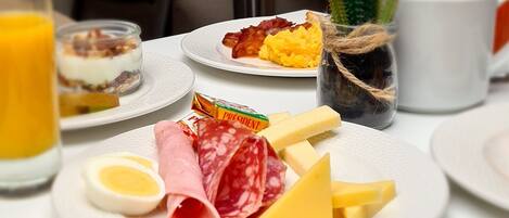 A breakfast setting with plates of food, including eggs, cheese, salami, and a jar of jam.