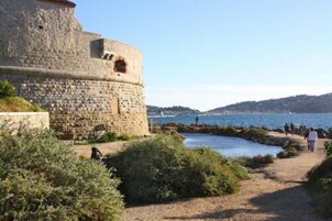 Una fortificación de piedra con una torre circular, un camino costero y vistas al mar.