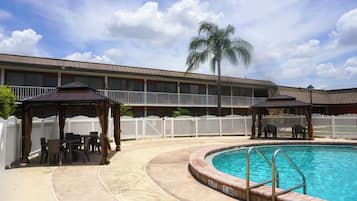 A hotel with a pool, outdoor seating, and a white picket fence.