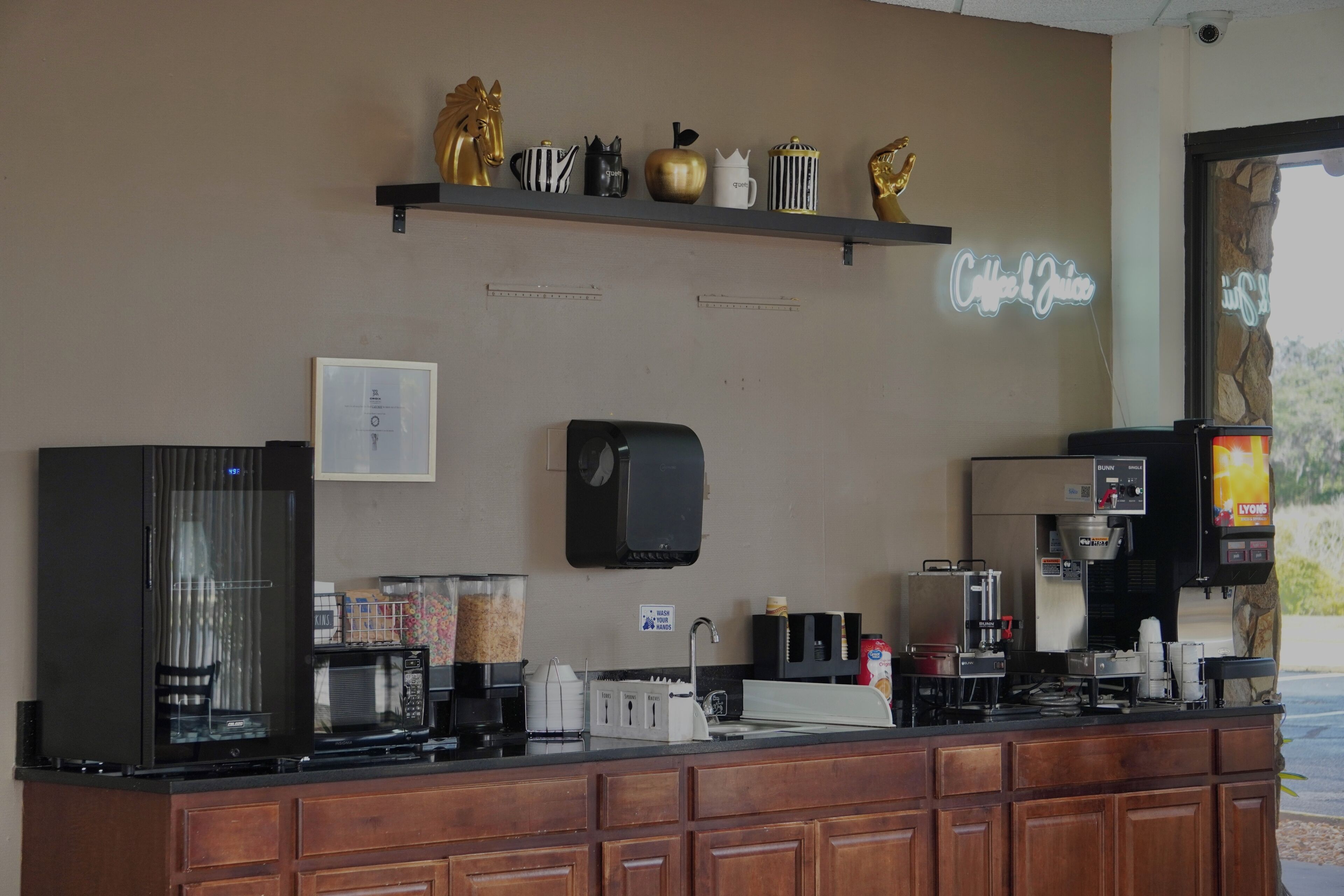 A coffee shop counter with a coffee machine, a microwave, a cash register, and a shelf with decorative items.