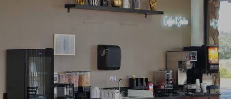 Ein Thekenbereich in einem Café mit einer Kaffeemaschine, einer Mikrowelle, einer Registrierkasse und einem Regal mit Dekoration.