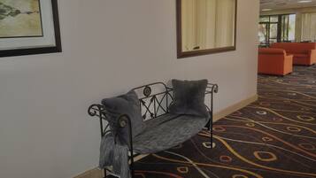 A corridor with a metal bench, a framed artwork, a mirror, and orange seating in the background.