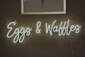 A neon sign with the words 'Eggs & Waffles' on a wall.