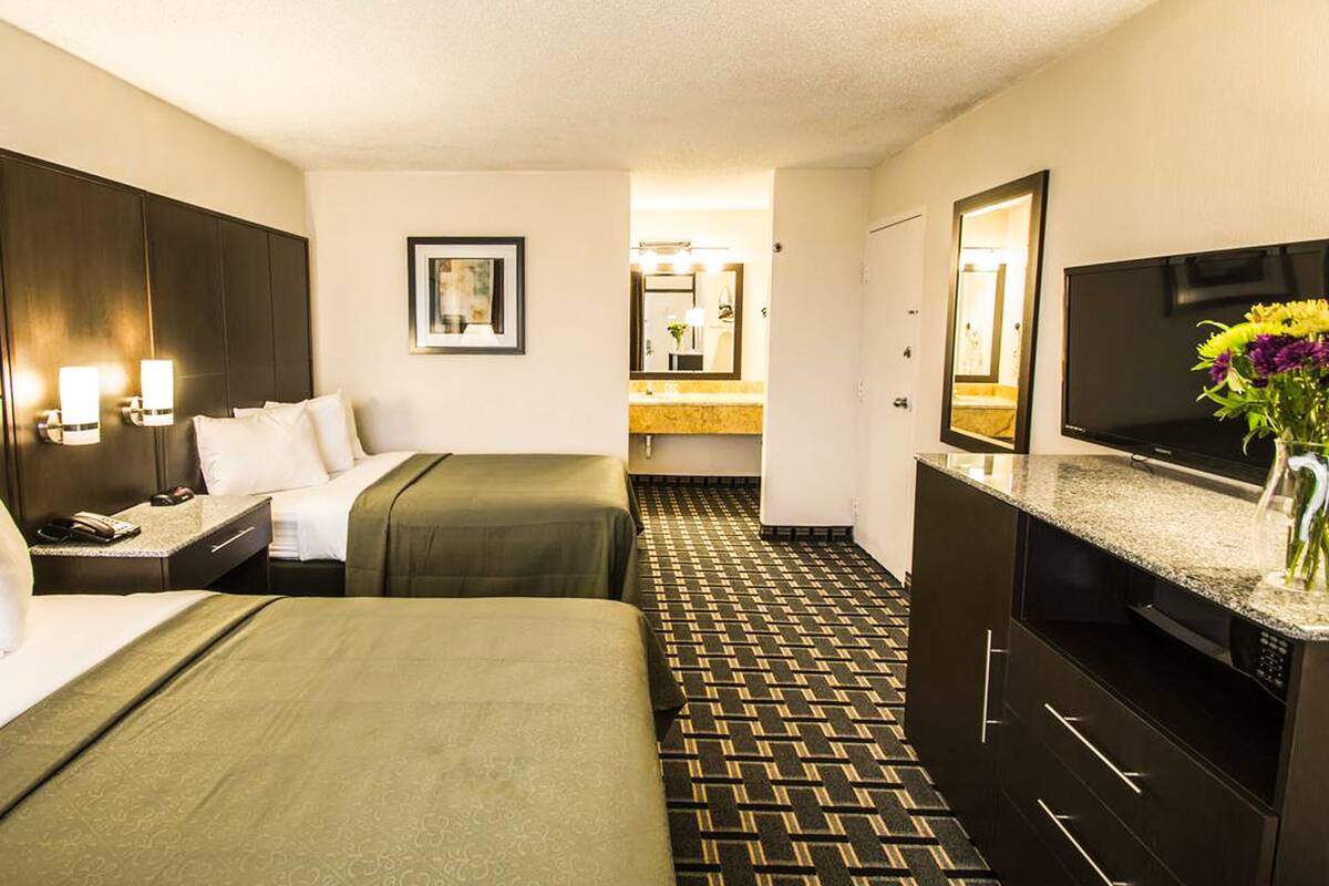 A hotel room with two beds, a TV, a bathroom, and a patterned floor.