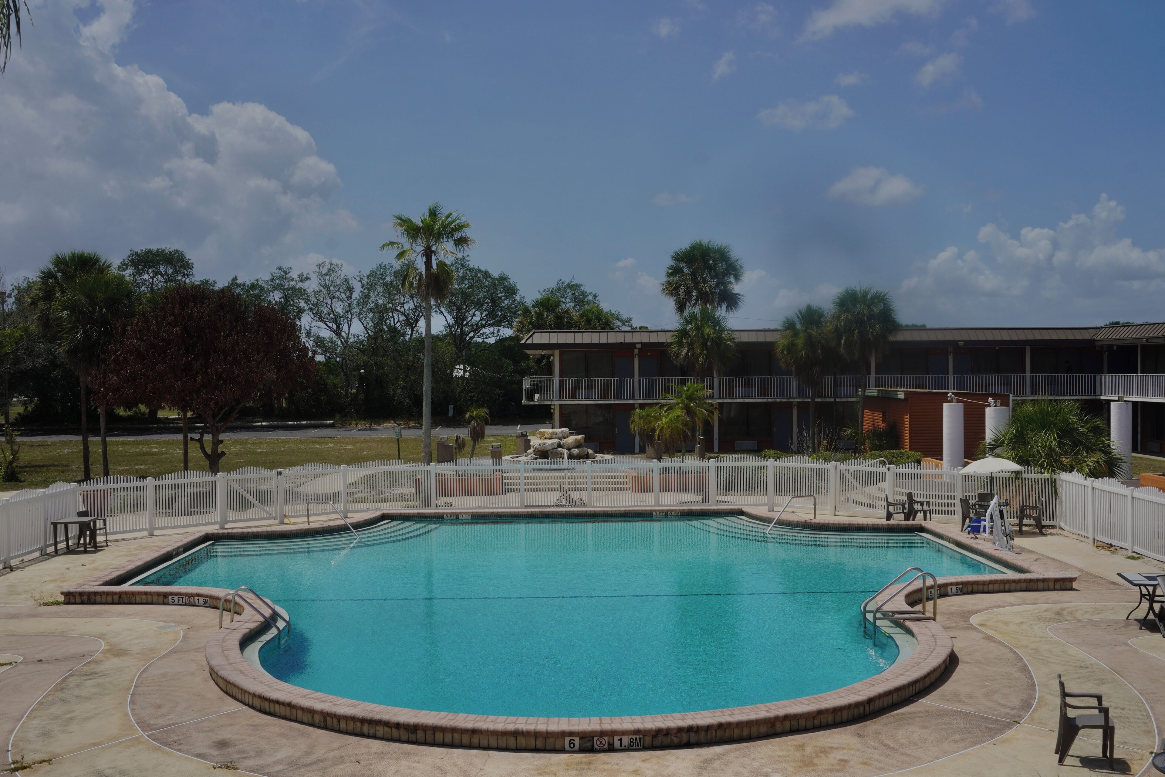 Una piscina con cerca blanca, palmeras y un edificio al fondo.