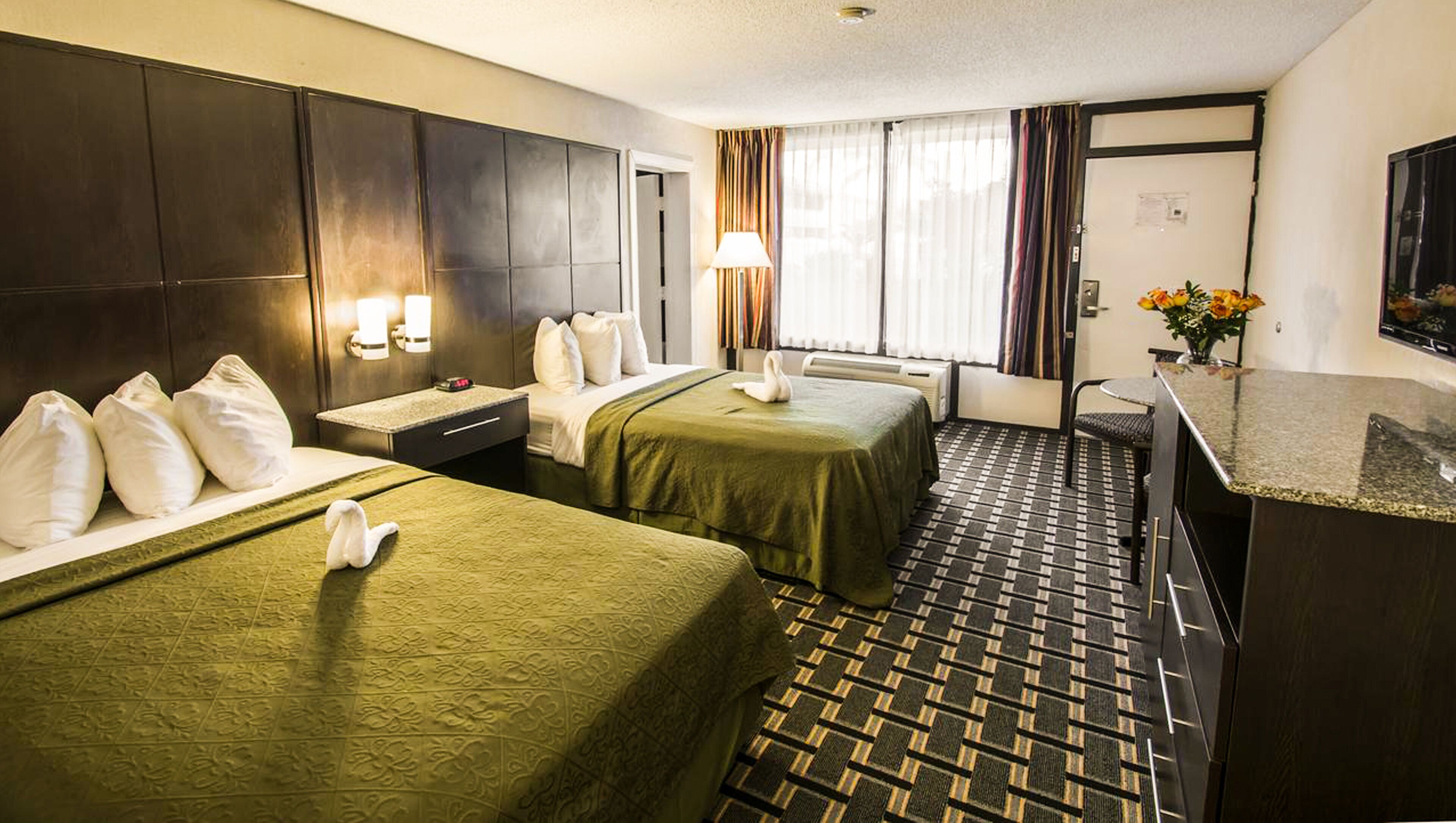 Ein Hotelzimmer mit zwei Betten, einem Schreibtisch, einem Stuhl, einer Lampe und einem kleinen Tisch mit Blumen.