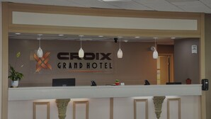 Een receptiebalie met een bordje waarop 'CROIX GRAND HOTEL' staat, een potplant en een telefoon.