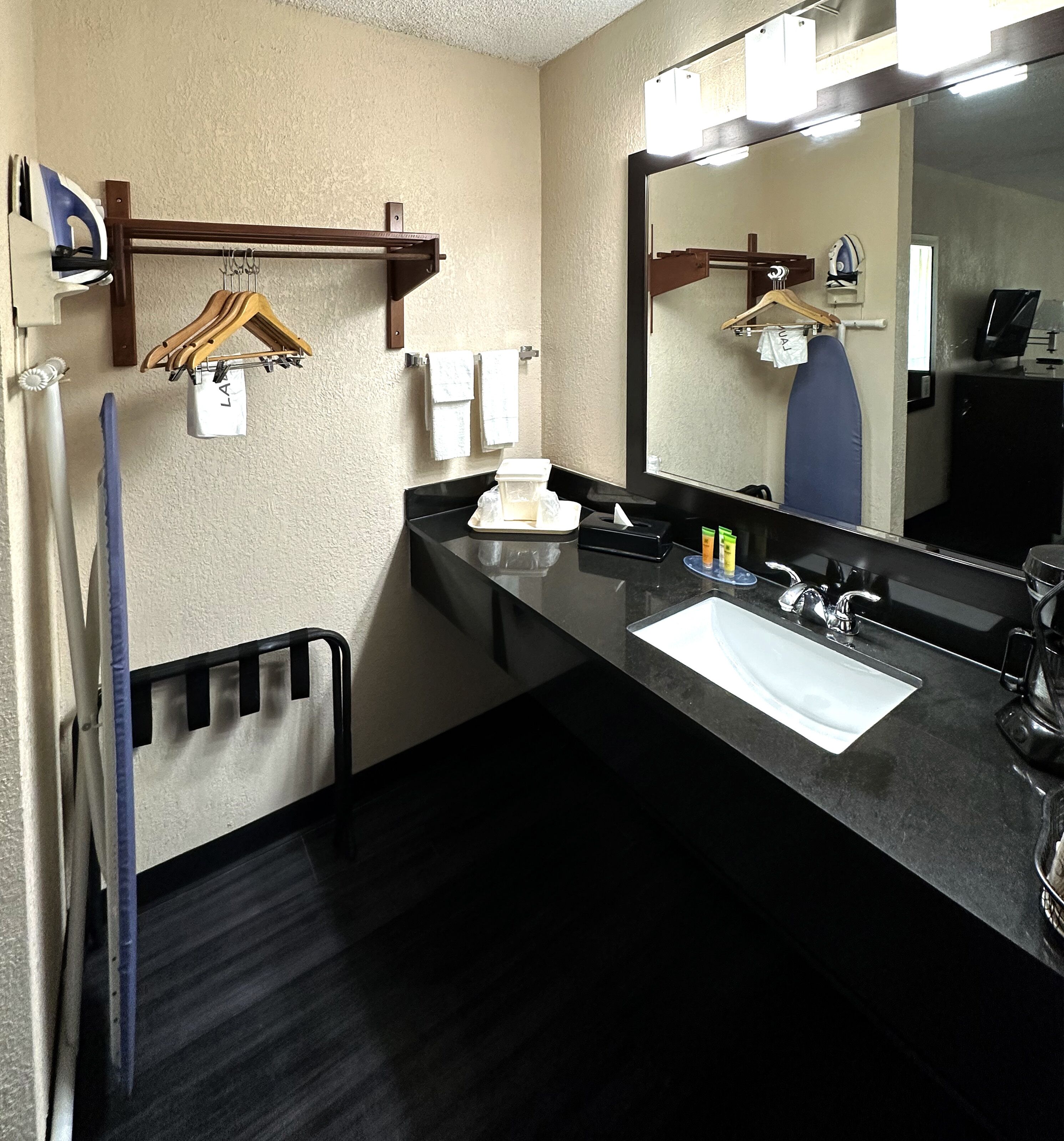 Une salle de bain d’hôtel avec un plan de toilette noir, un lavabo, un miroir et un porte-serviettes.
