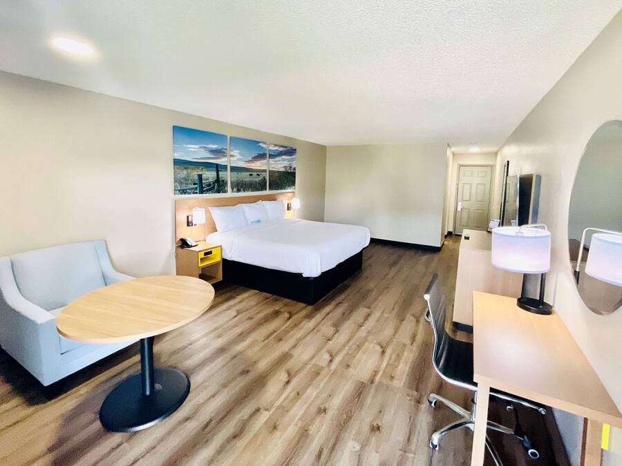 A hotel room with a bed, a desk, a chair, a round table, and a painting on the wall.